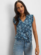 Blue and white shibori lilies print top with a V-neck and ruffled short sleeves, tucked into jeans.