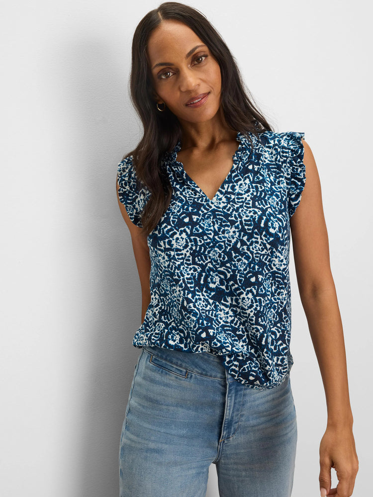 Blue and white shibori lilies print top with a V-neck and ruffled short sleeves, tucked into jeans.