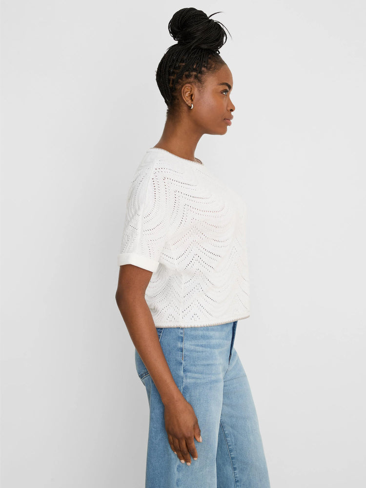 White short-sleeved sweater with open wavy swirl stitch pattern, rolled cuffs. Model wears light jeans.
