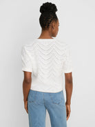 Off-white short-sleeve sweater with a wavy, open-knit swirl stitch pattern. Back view.