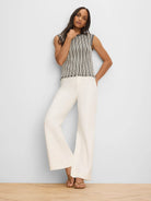 Sleeveless cream and black vertical striped sweater with a dark trim crew neck and fringed hem.