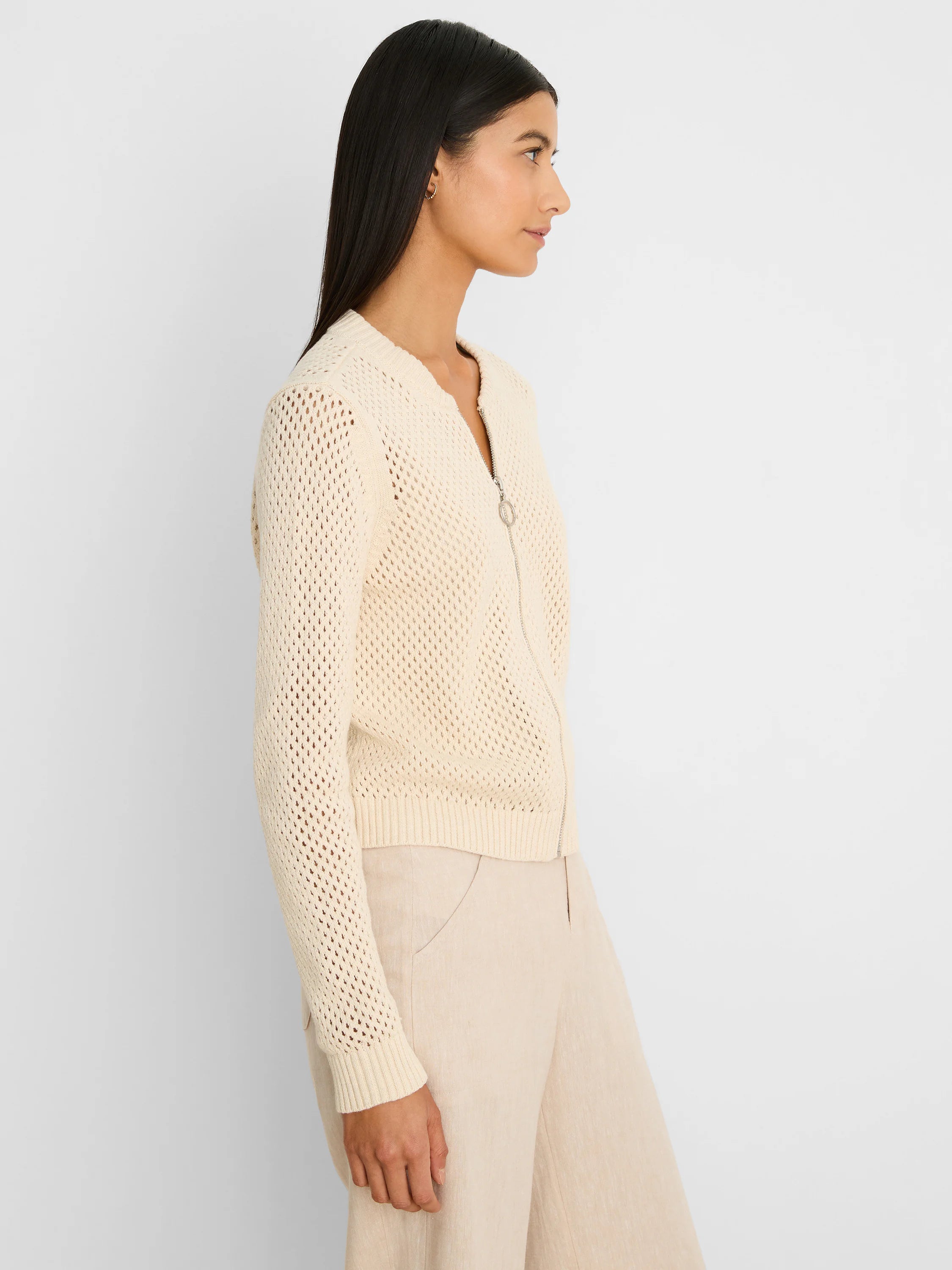 Cream open-knit zip-front cardigan with silver zipper pull, ribbed cuffs and hem, worn by a model.