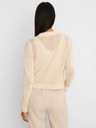Cream open-knit cardigan shown from the back, featuring ribbed cuffs and hem.