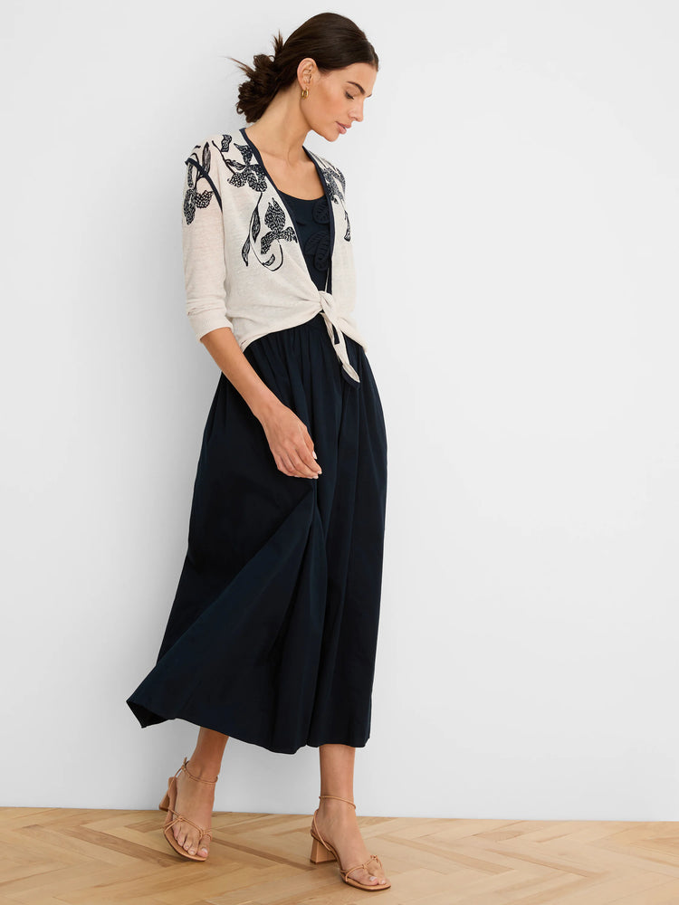 Off-white cardigan features dark floral pattern on shoulders & front. Model wears it tied over a navy dress.