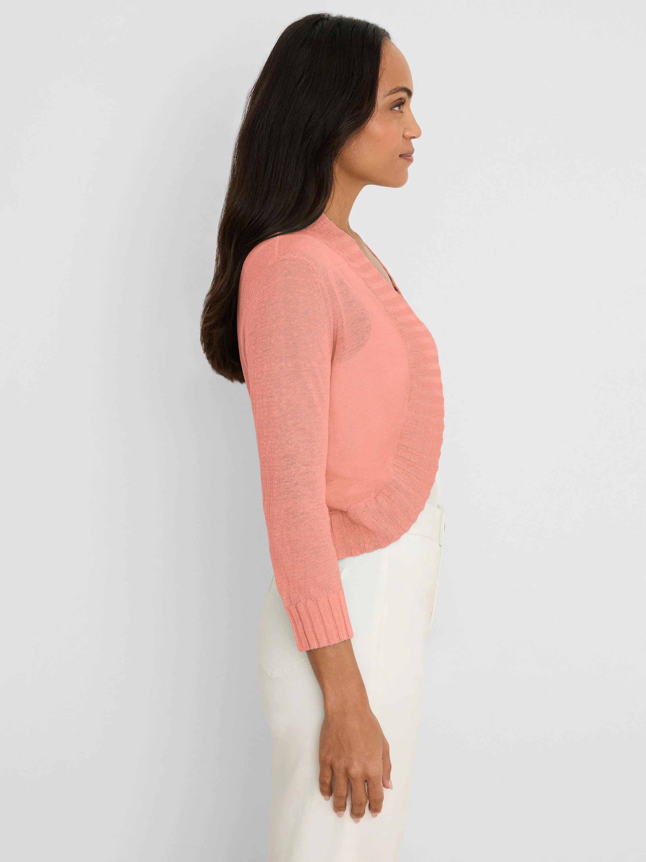 Peach bolero cardigan with V-neck, long sleeves, ribbed cuffs & hem. Worn open on model in side profile.