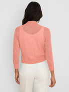 Peach knit bolero cardigan with mock neck, long sleeves, ribbed cuffs/hem, and semi-sheer fabric.