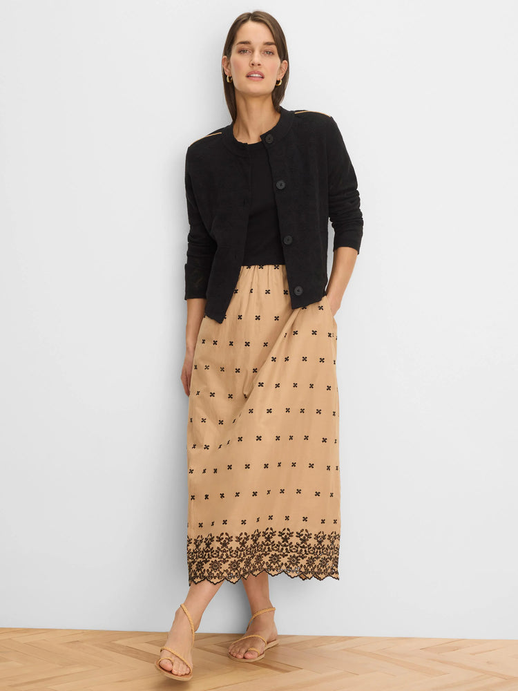 Tan embroidered dress with scattered black cross motifs and dense floral black embroidery at the scalloped hem.