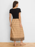 Black top, tan midi dress with scattered black clover embroidery, and a wide black floral embroidered hem.