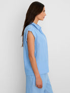 Light blue collared shirt with thin white vertical stripes and cuffed short sleeves. Model shown from side.