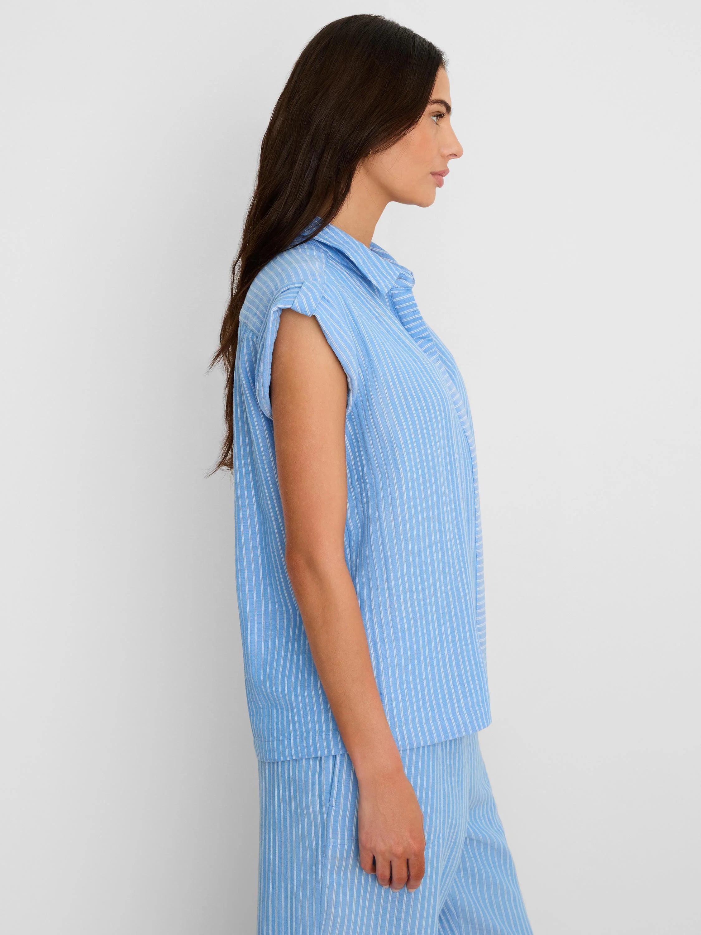 Light blue collared shirt with thin white vertical stripes and cuffed short sleeves. Model shown from side.