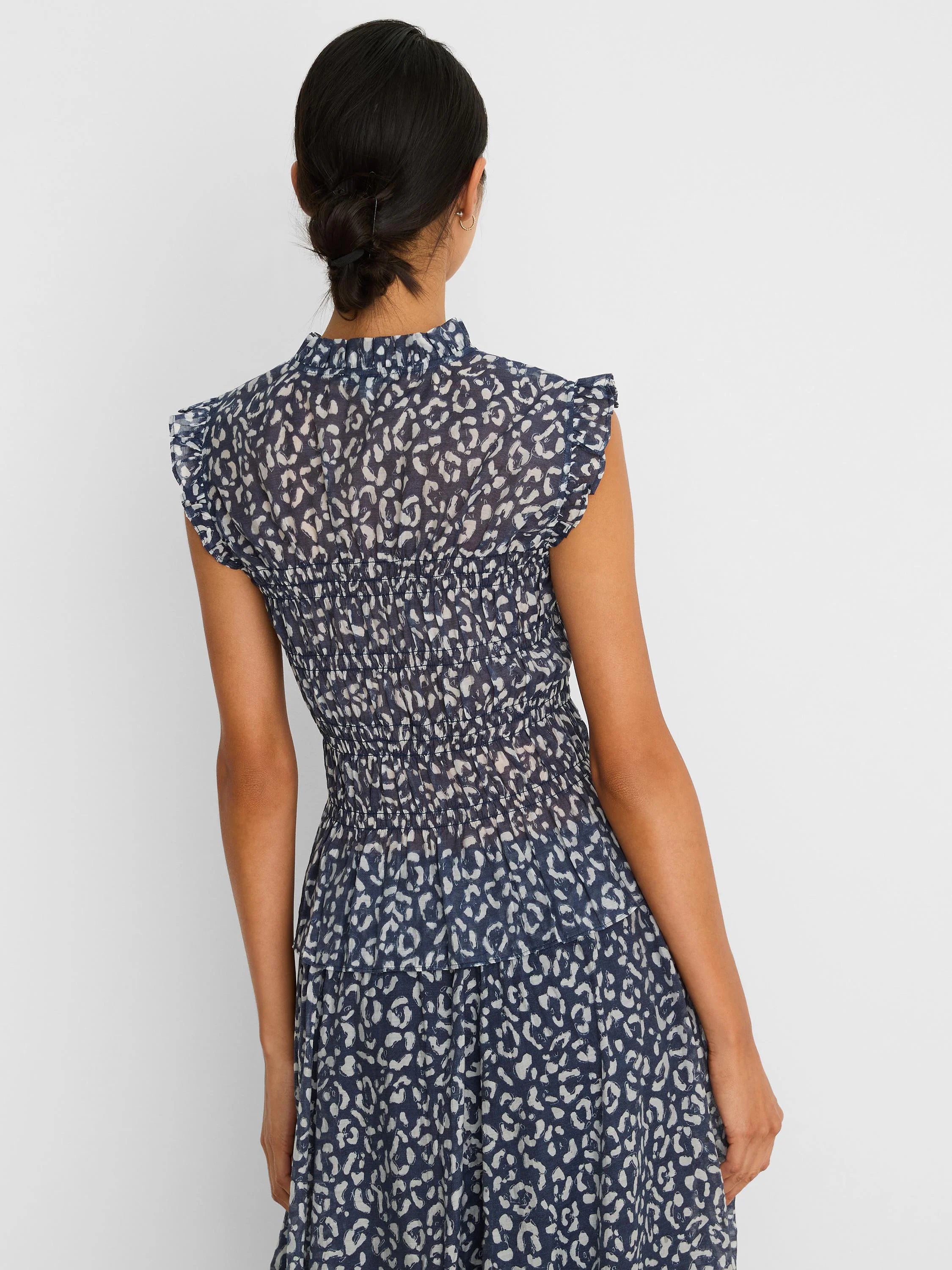 Indigo top with white abstract leopard print, smocked waist, ruffled mock neck, and cap sleeves.