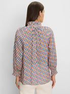 Back of woman in a pink, blue & tan geometric cotton crinkle shirt with ruffled neck and smocked cuffs.