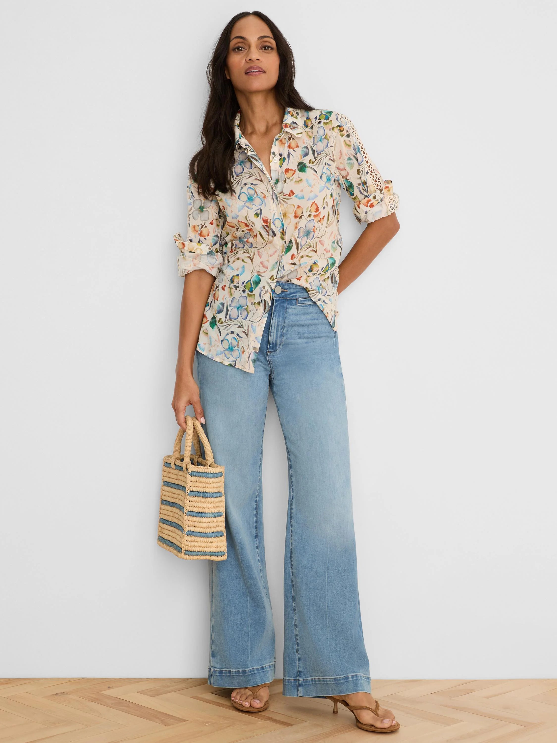 Cream button-down shirt with multi-colored pressed flower print in blue, orange, and green. Features eyelet details on...