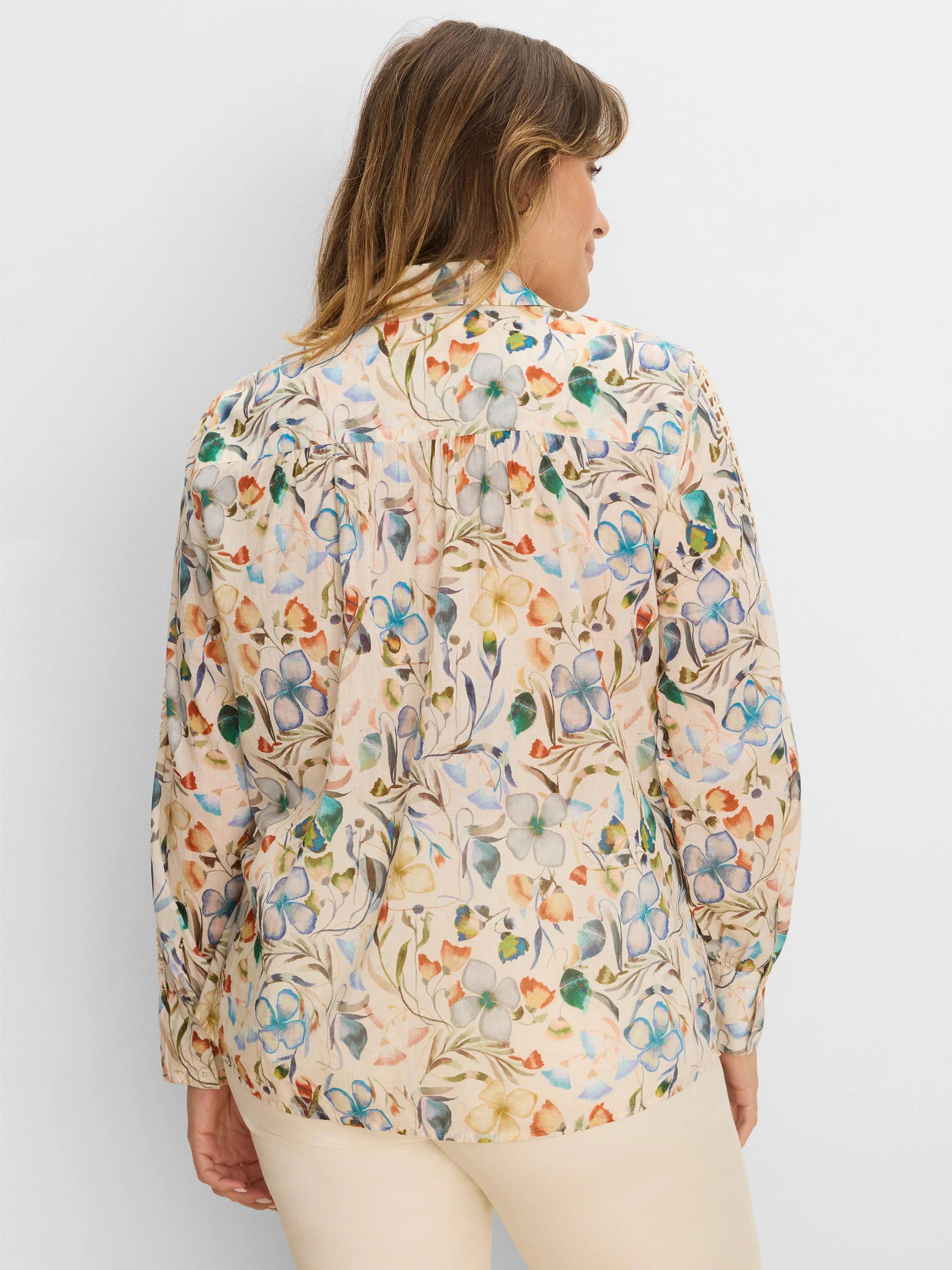 Back of a long-sleeved, light cream shirt with a multi-color floral pattern in blues, greens, and oranges.