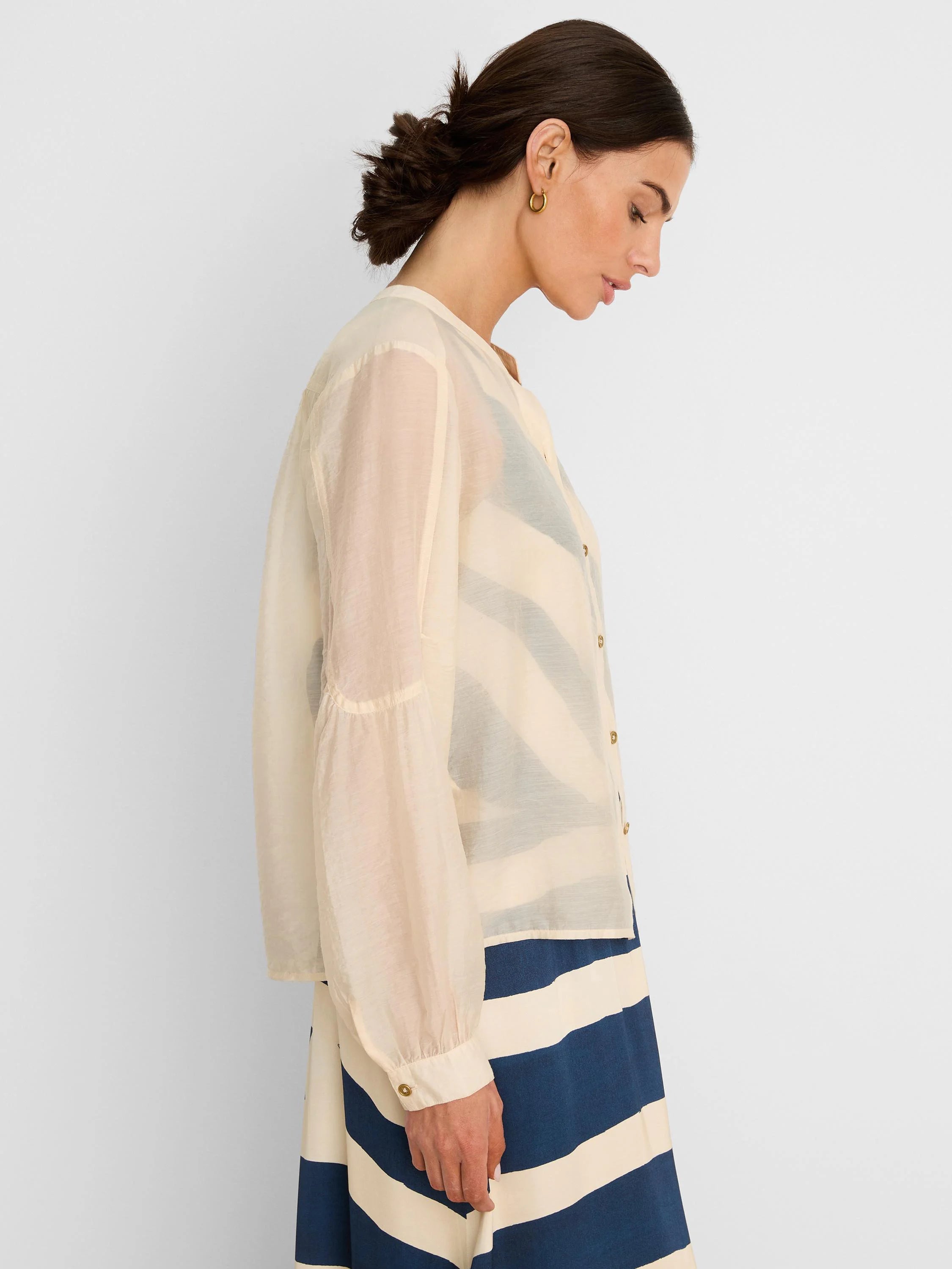 Sheer cream long-sleeve button-front shirt. A dark top and striped skirt are visible underneath.