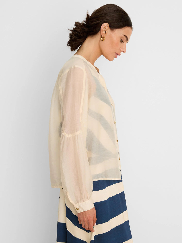 Sheer cream long-sleeve button-front shirt. A dark top and striped skirt are visible underneath.