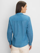 Blue long-sleeved cotton lawn shirt, back view. Features a collar, gathered back yoke, and curved hem.