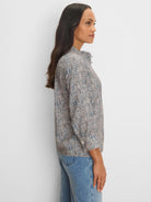 Light top, long sleeves, pale blue, tan & black speckled pattern, ruffled high neck.