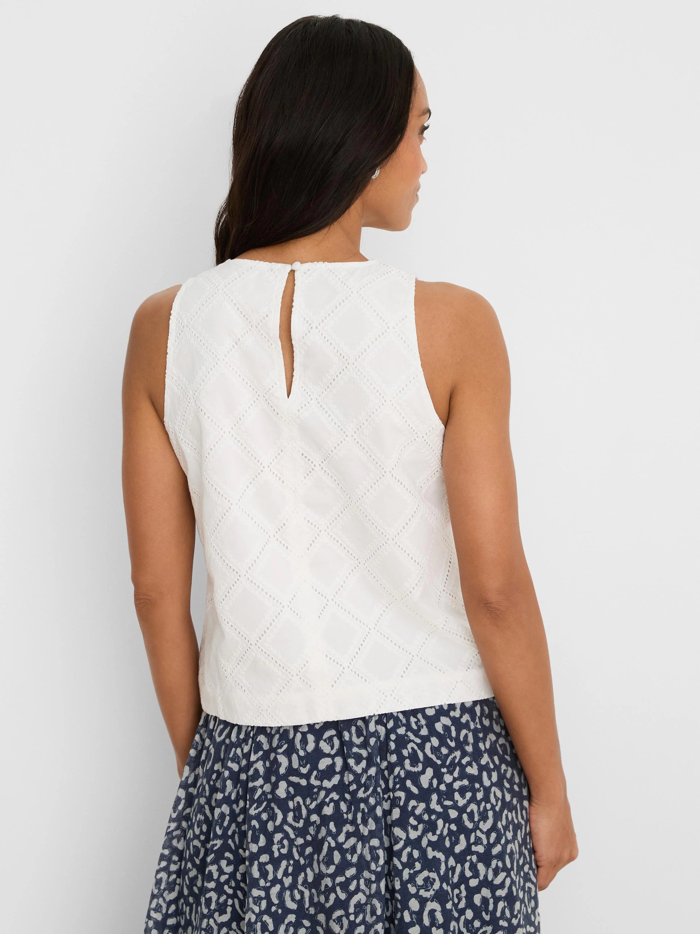 White sleeveless top with diamond eyelet pattern. Keyhole opening with button at back neck.