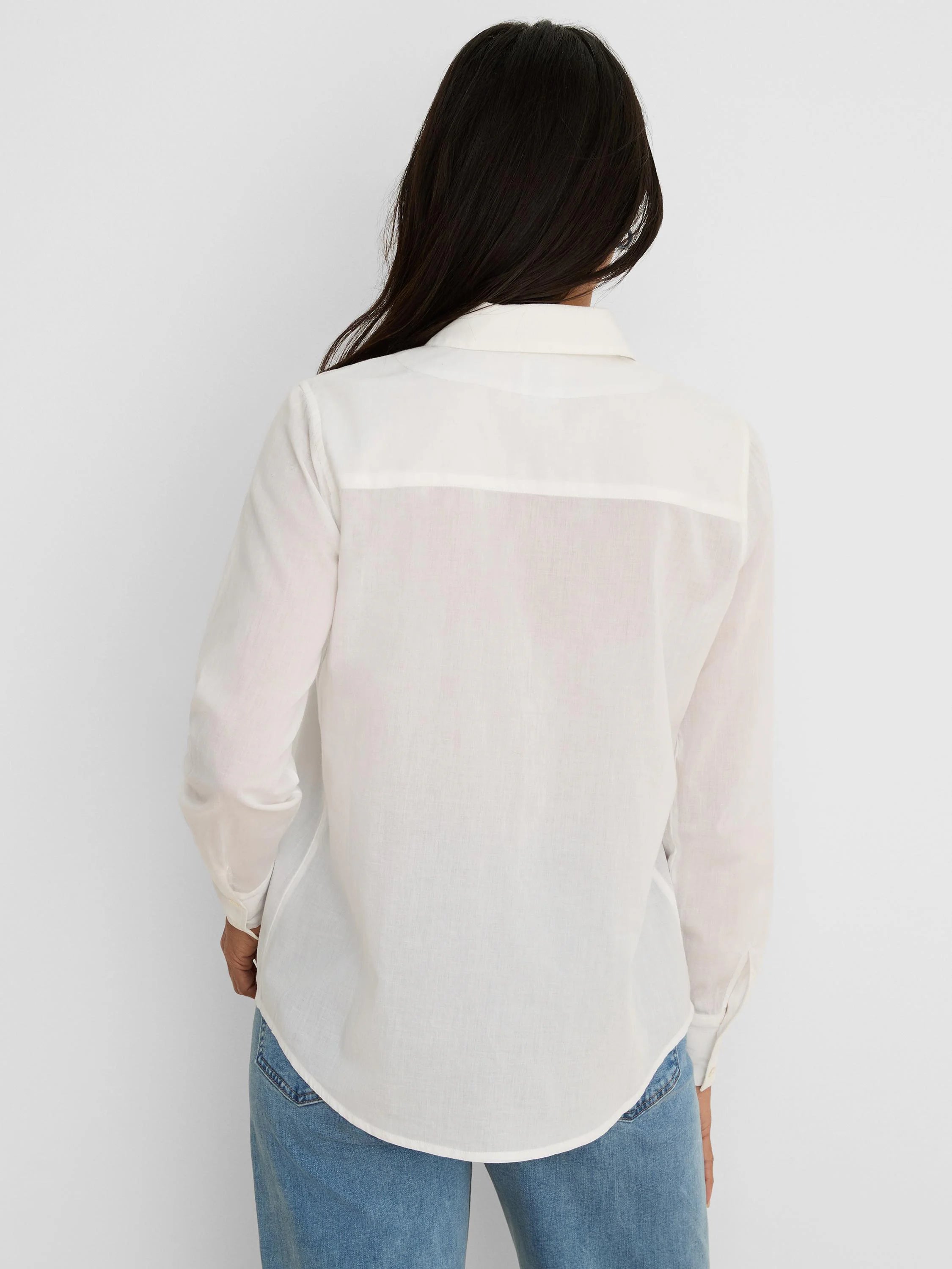 Back view of a white collared cotton shirt with long sleeves, buttoned cuffs, a back yoke, and a rounded hem.