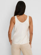 Off-white glossy tank top with white lace trim around the back scoop neckline, modeled from behind.