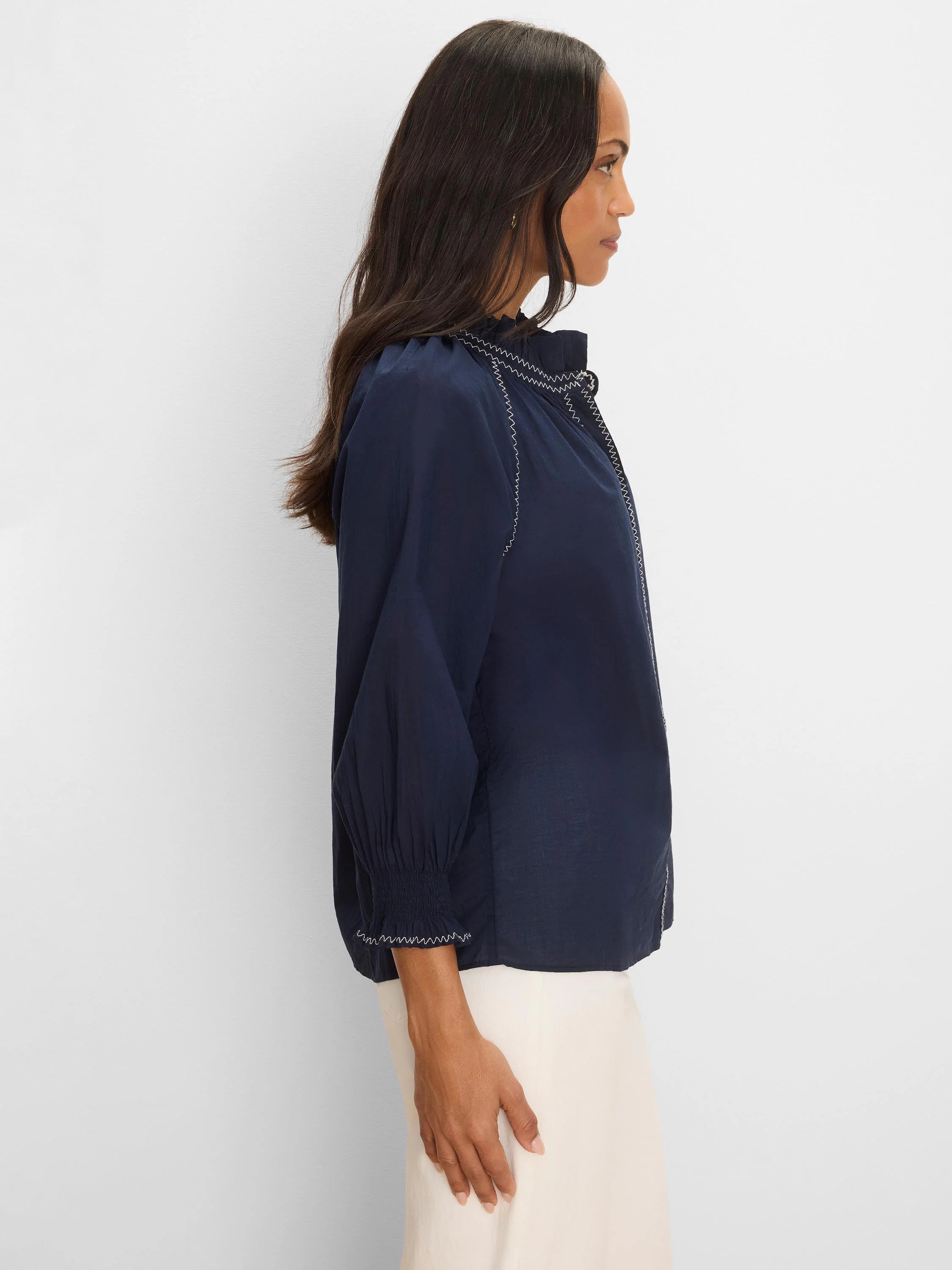 Navy crinkle shirt with white zig-zag stitching on a ruffled collar, raglan seams, and smocked cuffs.