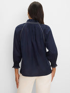 Navy blue crinkle shirt, back view. Features white zig-zag stitching on ruffled neckline, shoulder lines, and smocked cuffs.