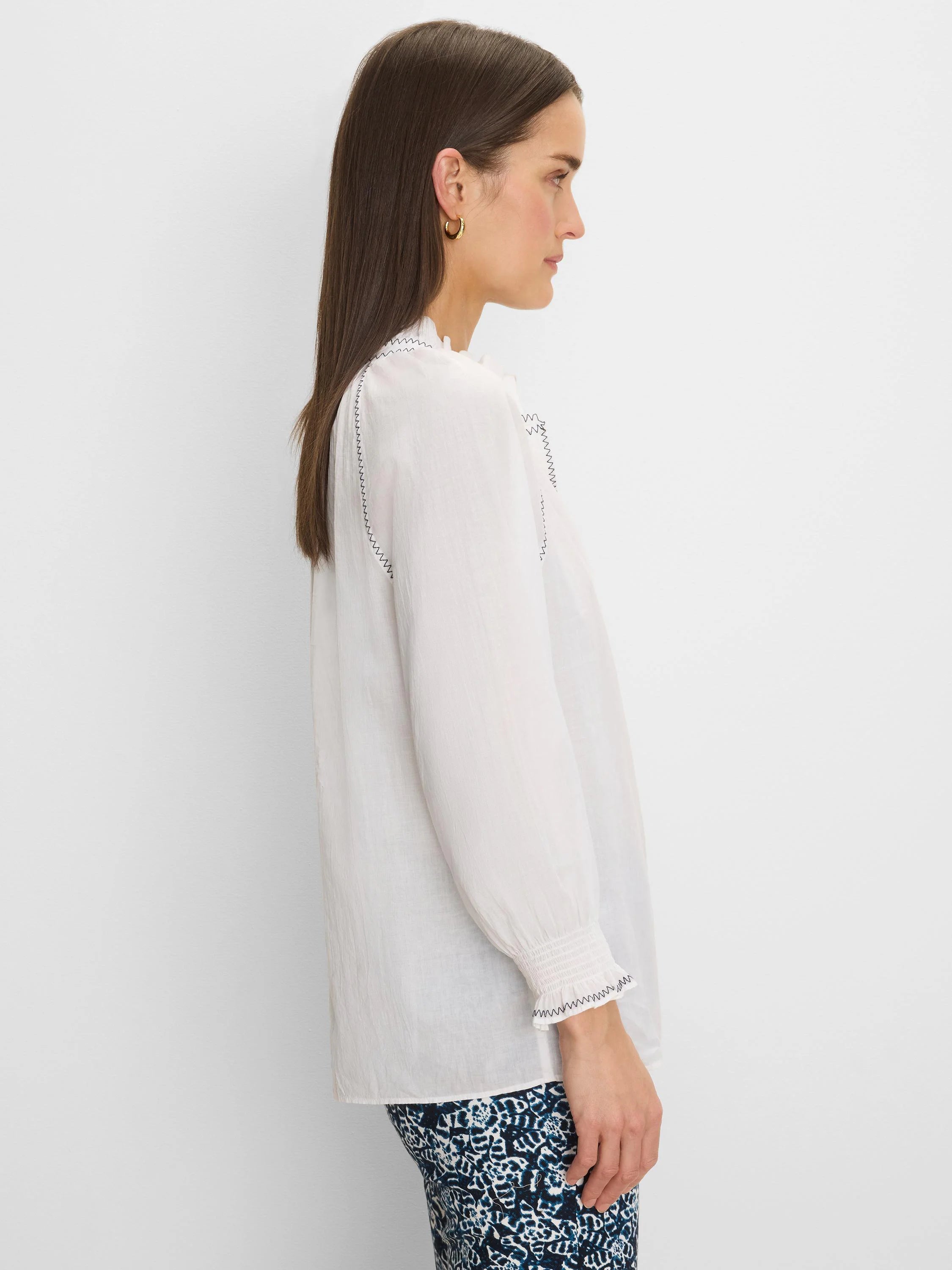 White crinkle cotton shirt with black zig-zag stitching on ruffled collar, shoulders, and smocked cuffs.