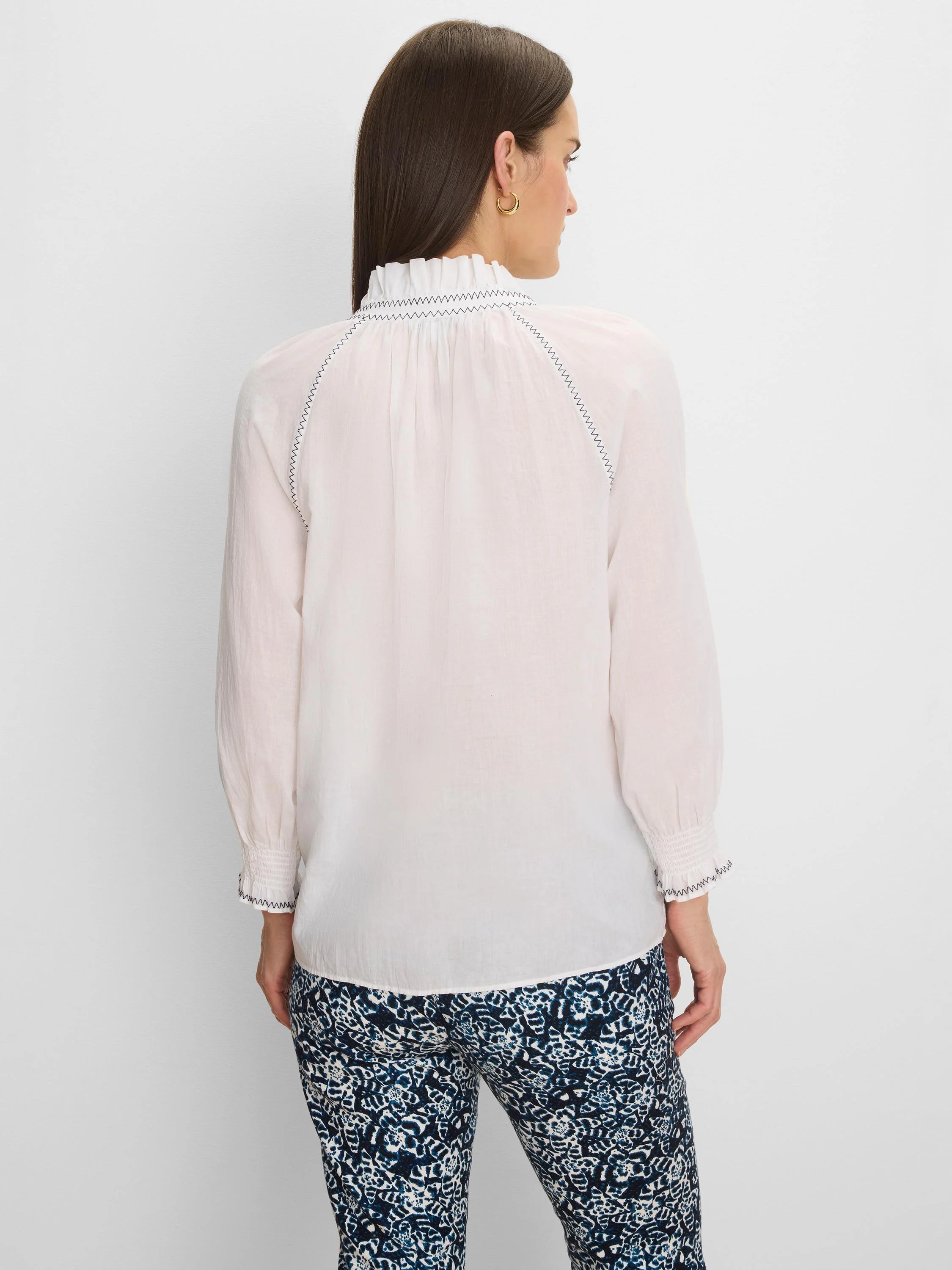 White crinkle shirt with dark zig-zag stitching on a ruffled high collar, back raglan seams, and smocked cuffs.