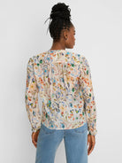 Cream shirt, back view, with multi-color pressed flower print (blues, oranges, greens). Long sleeves, gathered back yoke.