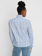 White shirt with blue tile embroidery. Features ruffled mock neck & long sleeves. Back view.