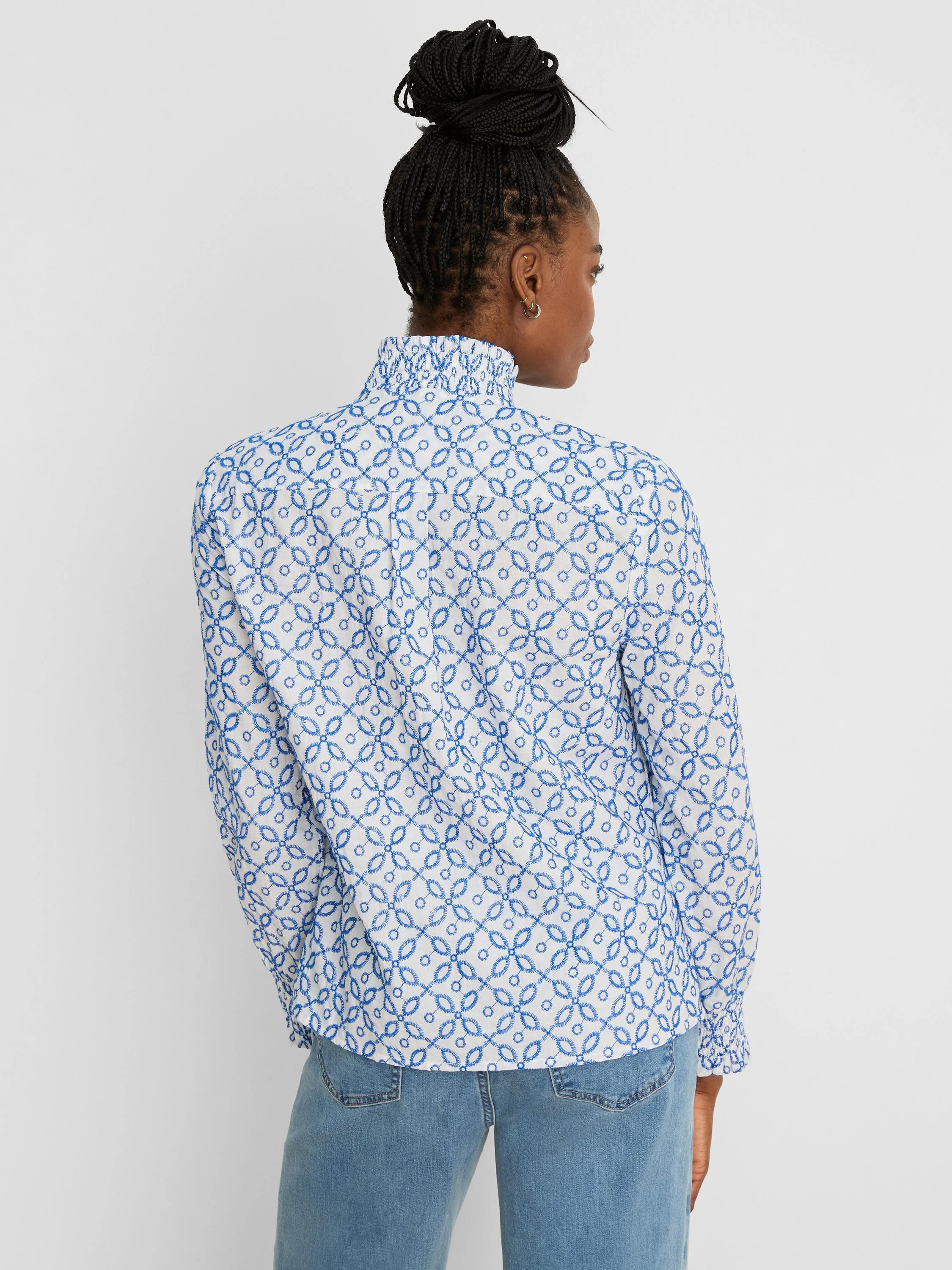 White shirt with blue tile embroidery. Features ruffled mock neck & long sleeves. Back view.