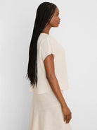 Light beige linen tee with short, wide sleeves, worn by a woman in profile.