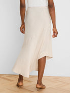 Light beige linen midi skirt, A-line with an asymmetrical hem and visible panel seams, shown from the back.