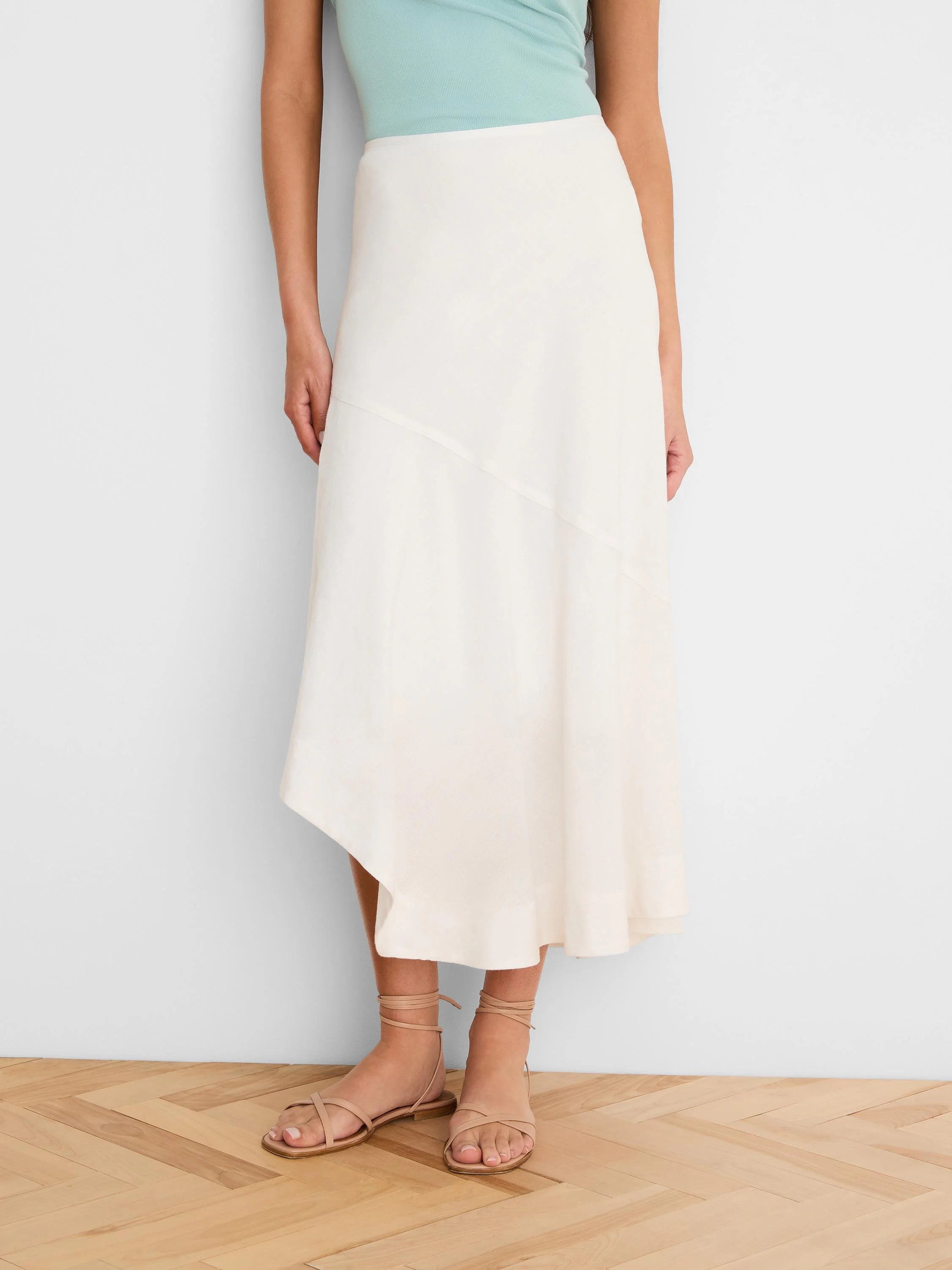 Off-white midi linen skirt with an asymmetric hemline and a diagonal seam detail.