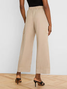 Beige wide-leg drapey cargo ankle pants with elastic waist and side cargo pockets, viewed from behind.