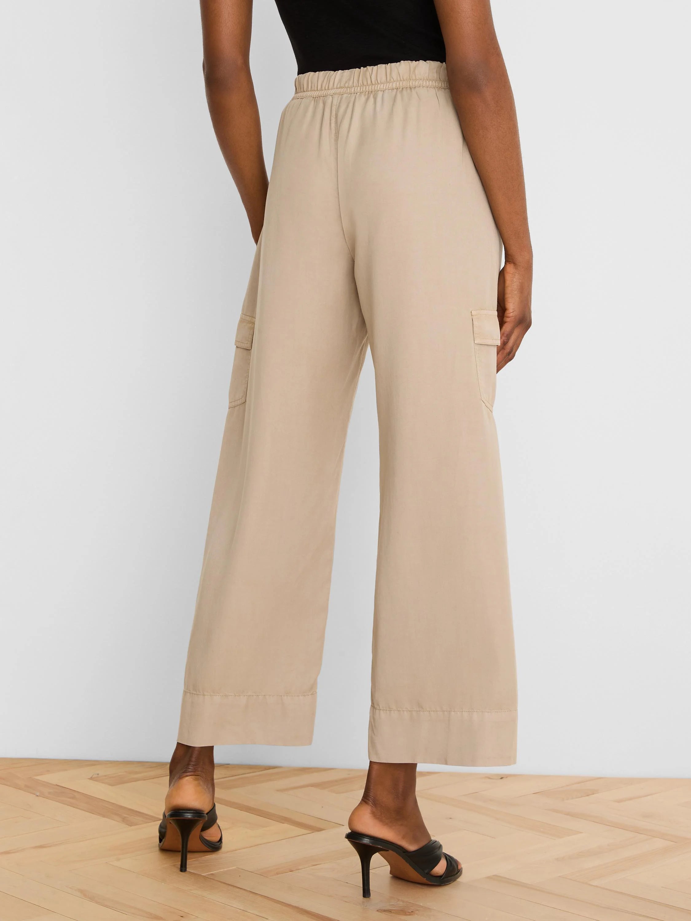 Beige wide-leg drapey cargo ankle pants with elastic waist and side cargo pockets, viewed from behind.