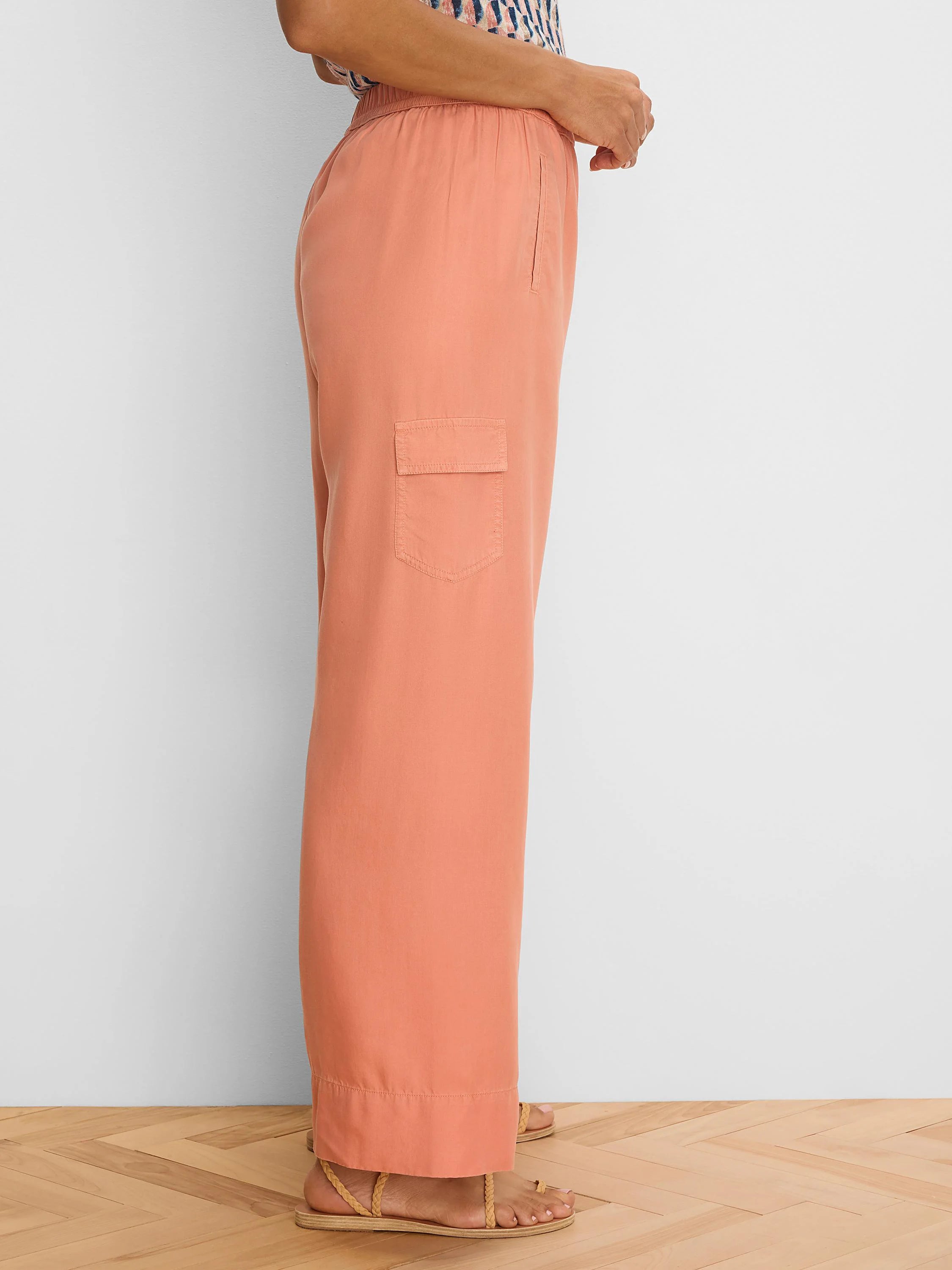 Peachy-orange wide leg drapey cargo ankle pants. Features an elastic waist, side slit pocket, and flap cargo pocket.