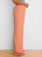 Peachy-orange wide leg drapey cargo ankle pants. Features an elastic waist, side slit pocket, and flap cargo pocket.