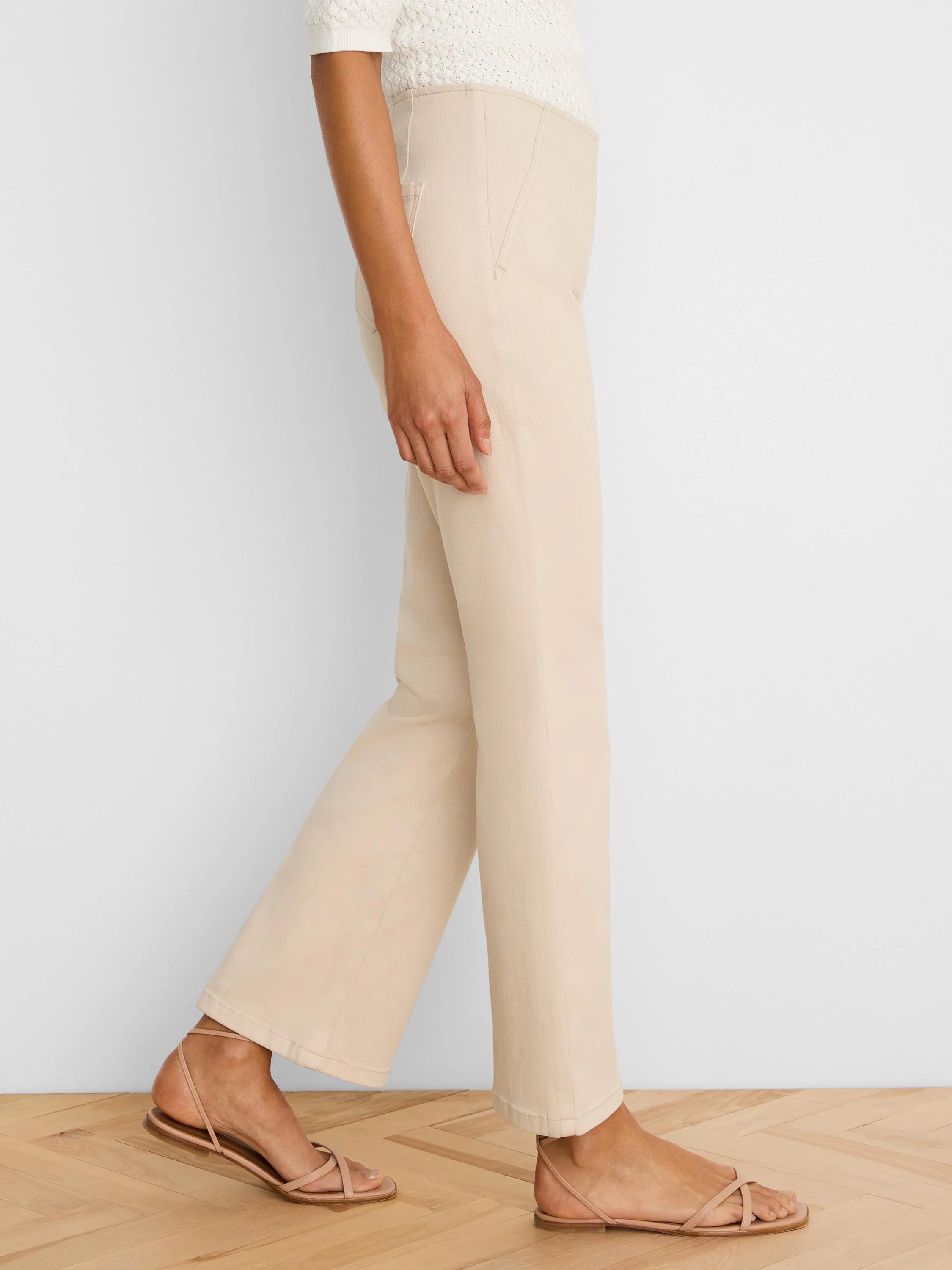 Light beige boot-cut jeans, side view on a model, fitted through thigh, subtle flare at hem.