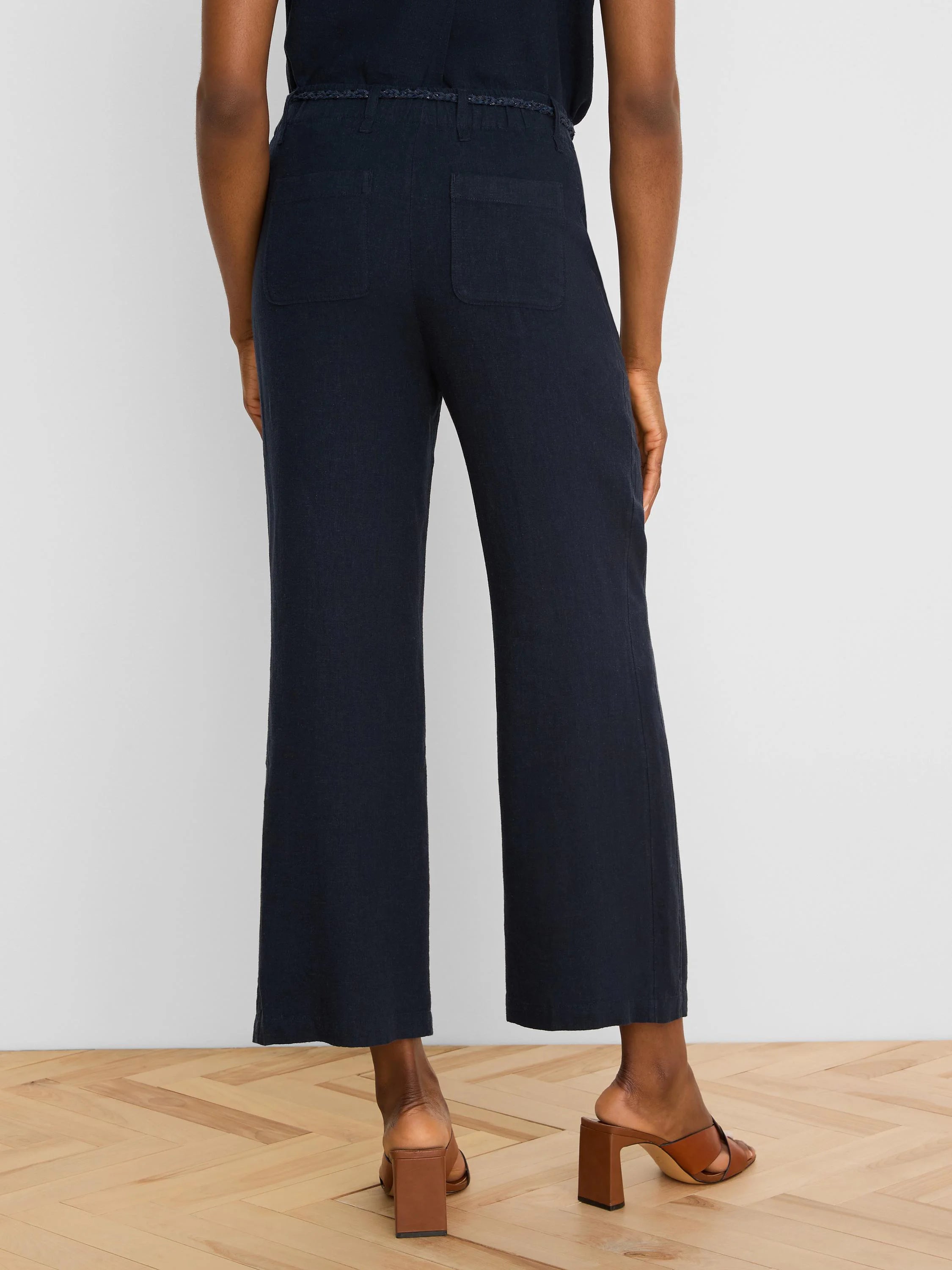 Navy wide-leg linen crop pants with a braided self-belt and two large rear patch pockets, viewed from behind.