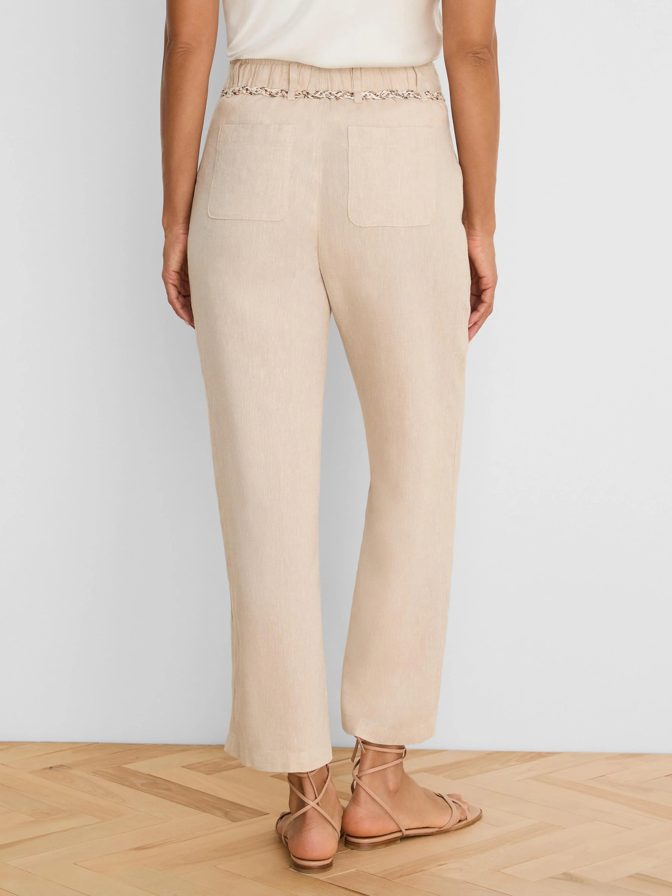 Beige wide-leg linen crop pants, seen from behind. Features a braided belt and two back patch pockets.