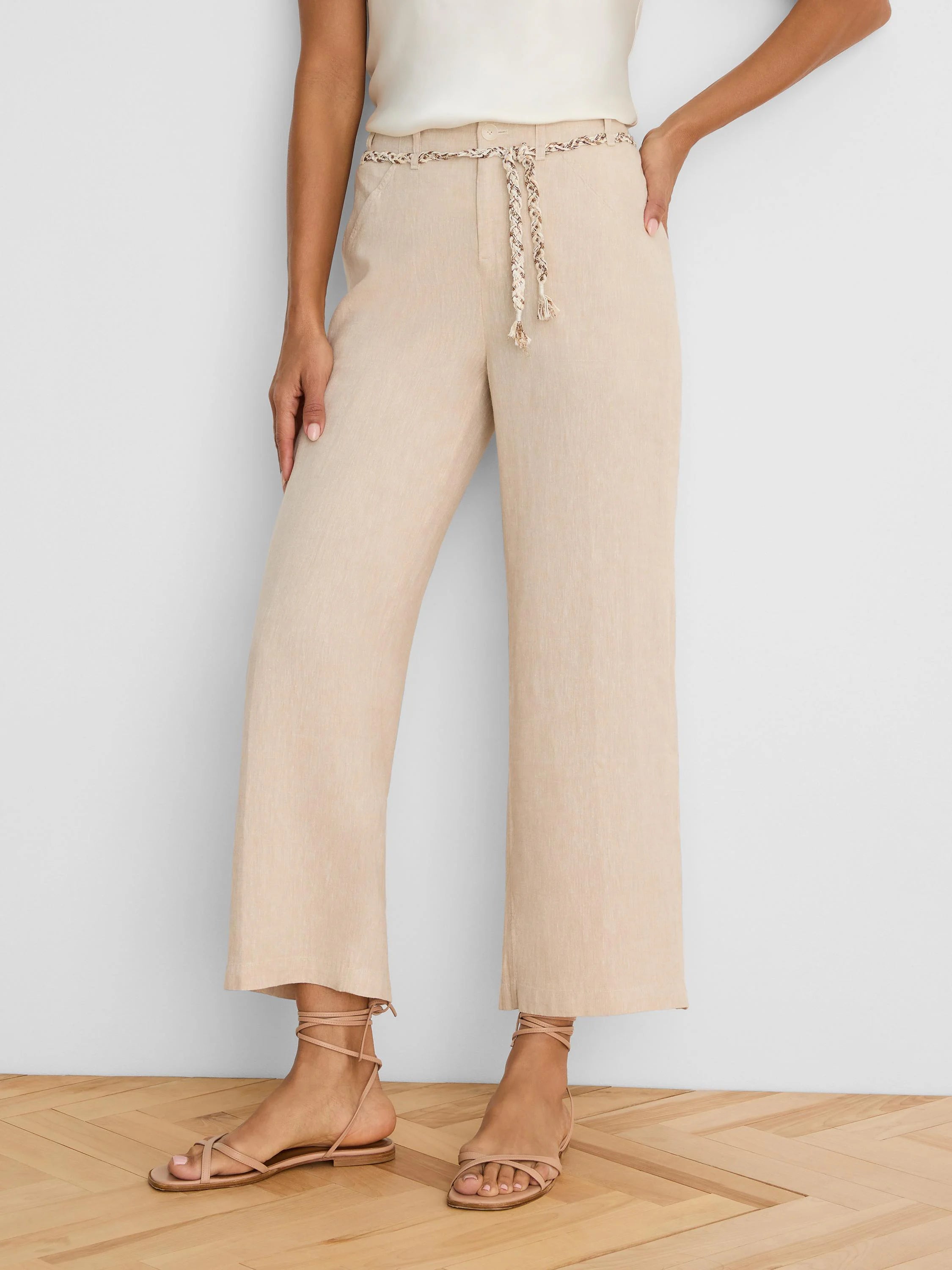 Light beige wide-leg linen crop pants feature a braided beige and brown patterned belt at the waist.