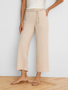 Light beige wide-leg linen crop pants feature a braided beige and brown patterned belt at the waist.