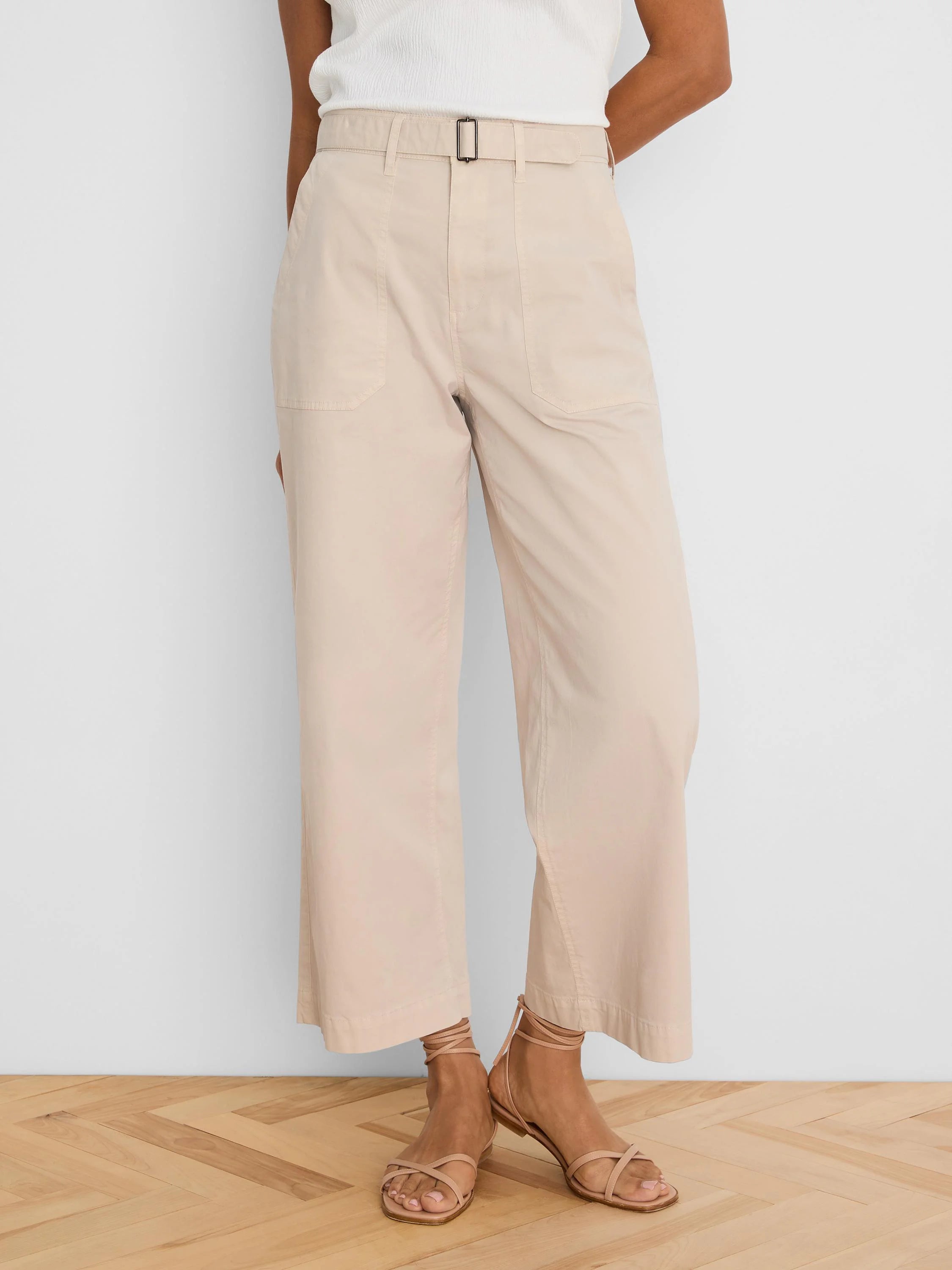 Light beige wide-leg ankle pants with a belted waist, dark rectangular buckle, and large front patch pockets.