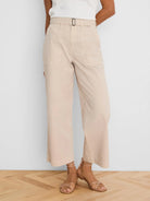 Light beige wide-leg ankle pants with a belted waist, dark rectangular buckle, and large front patch pockets.