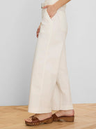 Cream wide-leg ankle pants with a matching belt and front slash pockets. Model's hand in pocket.