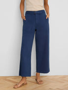 Dark blue wide-leg ankle pants with belted waist, front patch pockets, modeled on a person.