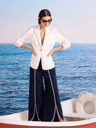 Dark blue wide-leg pants with white piping vertically down legs and outlining curved split seams at the hem.