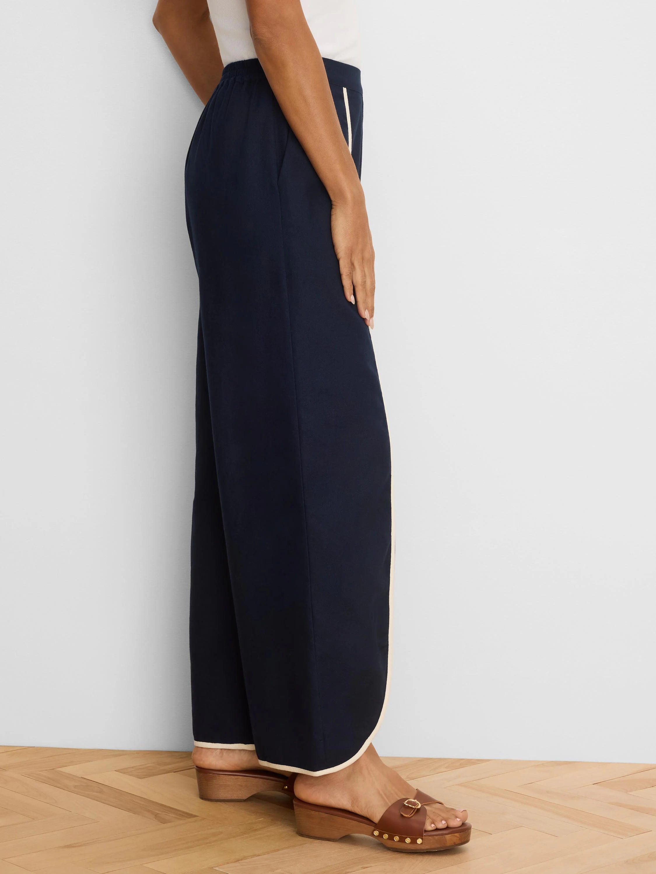 Dark navy wide leg pants, shown from side, with cream piping down side seams and around hems.
